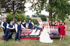 a group of people standing around a race car posing for a photo with the bride and groom