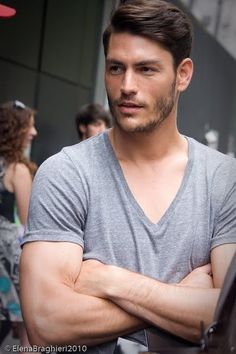 a man with his arms crossed standing in front of a group of people on the street