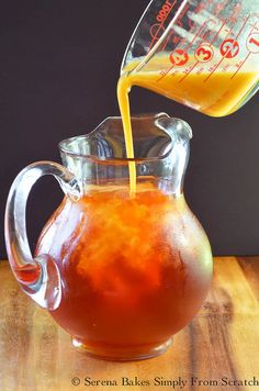 a pitcher filled with orange juice being poured into a glass pitcher on top of a wooden table