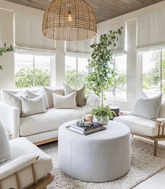 a living room filled with white furniture and lots of greenery on the windowsill