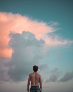 a man standing on top of a beach next to the ocean under a cloudy sky