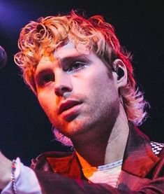 a young man with blonde hair holding a microphone in his right hand and looking off into the distance