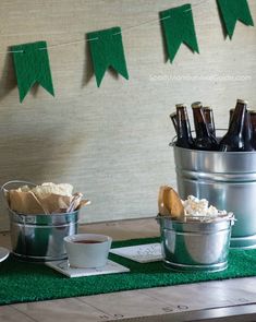 a table topped with two buckets filled with food and drinks next to bunting flags