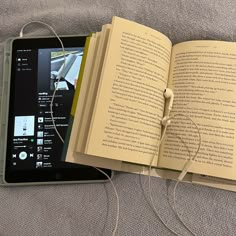 an open book sitting on top of a bed next to headphones and a tablet