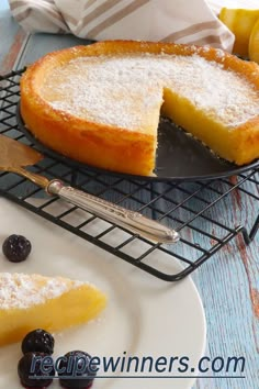 a lemon and blueberry cake on a cooling rack with a slice missing from it