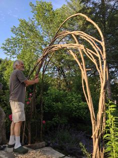 an older man is working on a garden arch made out of branches and twigs in his backyard