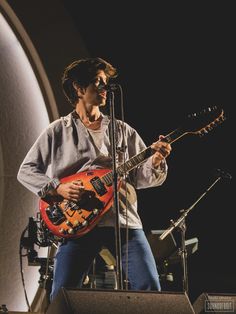 a man with a guitar standing in front of a microphone