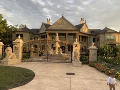 a young child standing in front of a gated entrance to a large house with statues on it