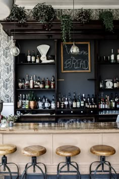 a bar with stools in front of it and bottles on the wall behind it