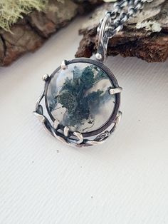 A round moss agate has twisting silver vines twining around its bottom curves. The translucent stone has deep green mossy inclusions that wisp throughout the center of the agate. A silver frame with prongs hold the agate so that the most amount of light can filter through this unique stone.  The silver has been oxidized and given a brushed finish to highlight the textures. Flying Crow, Goth Wedding, Metalwork Jewelry, Agate Jewelry, Moss Agate, Silver Frame, Deep Green, Earring Necklace, Ring Necklace