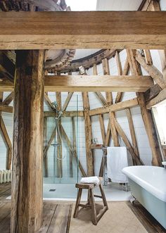 a bathroom with wooden beams and a white bathtub in the corner, along with a stool