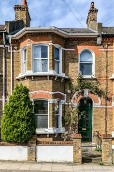 an old brick house with white trim and green doors on the front, surrounded by greenery