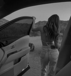 a woman standing in front of a car with her hand on the open door window