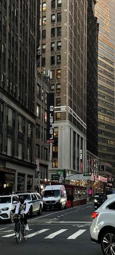 a city street filled with lots of tall buildings next to parked cars and people on bicycles