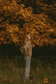 a woman standing in front of a tree with yellow leaves