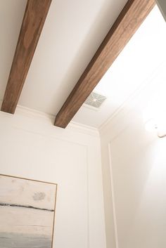 a painting is hanging on the wall next to a wooden beam in a white room