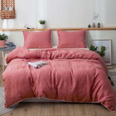 a bed with pink sheets and pillows in a white room next to a wooden table