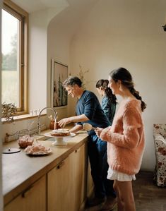 two people are preparing food on the counter in front of a window, while another person watches