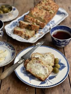 bread and olives are on plates next to tea cups, with two serving utensils