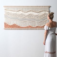 a woman is standing in front of a wall hanging with crochet on it