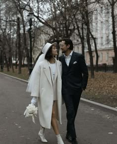 a bride and groom are walking down the street in their wedding attire, dressed in white