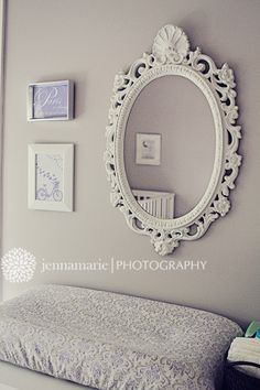 a white bed sitting under a mirror next to a wall with pictures hanging on it