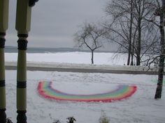 a rainbow painted object in the snow by some trees and water with no leaves on it