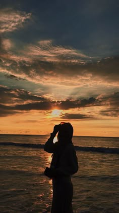 a woman standing on top of a beach next to the ocean under a cloudy sky