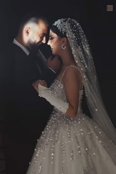 a bride and groom standing together in front of a dark background wearing wedding gowns