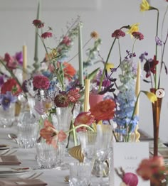 there are many vases with flowers in them on the long dining table set for an event