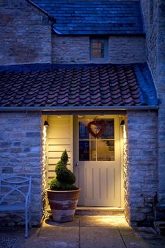 the front door of a house lit up with lights and potted plants on either side