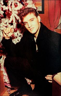 a man sitting in front of a christmas tree with his hand up to the camera