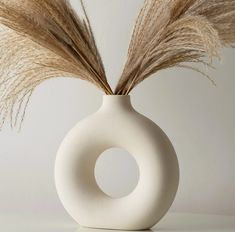 a white vase with some dry grass in it's center and two brown feathers sticking out of the top