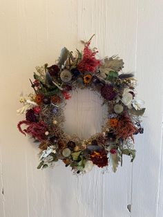 a wreath hanging on the side of a white door with dried flowers and greenery