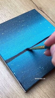 a hand holding a pair of scissors over a blue notebook with white speckles