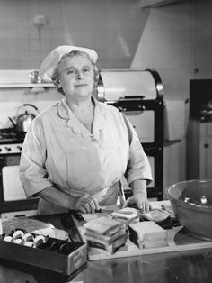 an old woman is standing in the kitchen with food on the counter and she is wearing a chef's hat