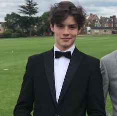 two men in tuxedos standing next to each other on a grass covered field