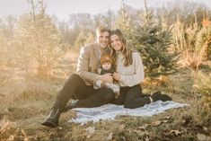 a man and woman are sitting on a blanket in the woods holding a baby boy