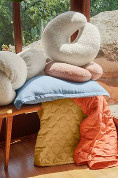 several pillows stacked on top of each other in front of a window with trees outside