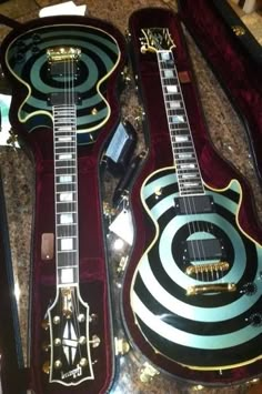 two guitars sitting on top of a table next to each other in cases with black and white designs