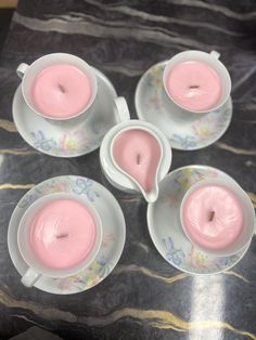 four tea cups and saucers with pink candles in them