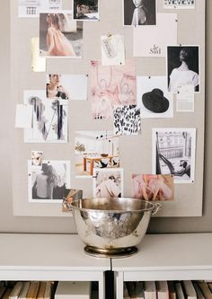 a silver bowl sitting on top of a white table next to a wall covered in pictures