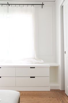 an empty bedroom with white furniture and curtains on the window sill, next to a bed