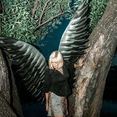 a woman standing next to a tree with large wings