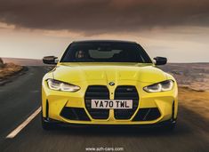 the front end of a yellow sports car driving down a road with dark clouds in the background