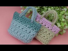 two crocheted purses sitting next to each other on a pink surface with flowers in the background