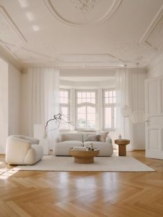 a living room filled with white furniture and wooden flooring next to a large window