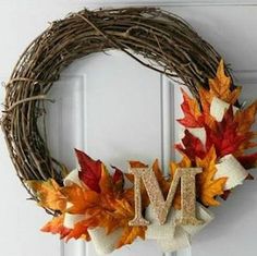 a wreath with the letter m on it and fall leaves hanging from it's front door