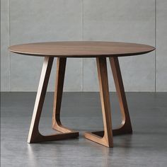 a round wooden table sitting on top of a cement floor next to a white wall