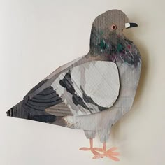 a bird made out of paper sitting on top of a white wall